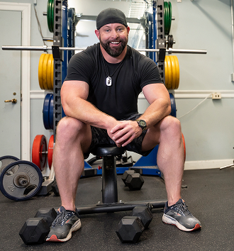 male Veteran in black shirt and shorts sitting on a bench
press at the gym